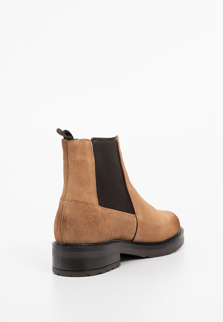 Bota Chelsea de ante marrón con panel lateral elástico negro, puntera redondeada y suela gruesa negra. Incluye una lengüeta en la parte trasera.