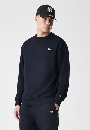 Black sweatshirt with a round neck and ribbed cuffs. Features a small white logo on the chest and matching pants with a similar logo.