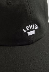 Une casquette en coton noir avec un logo "LEVİS" brodé en blanc à l'avant. Le design comprend une visière incurvée et un tissu texturé.
