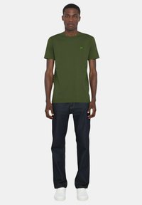 T-shirt verde oliva a maniche corte con scollatura rotonda e piccolo logo. Abbinato a jeans blu scuro e sneakers bianche.