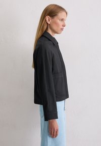 Czarna krótka kurtka z kołnierzem, o strukturze i bocznych kieszeniach. Gładka faktura z widocznymi detalami szwów.