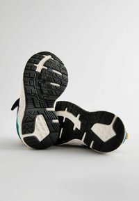 Buty sportowe z czarną gumową podeszwą zewnętrzną z wzorami trakcyjnymi, białą podeszwą środkową i akcentami w kolorze teal po bokach.