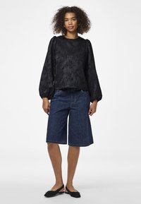 Blusa nera a maniche lunghe con motivo floreale testurizzato, abbinata a pantaloni shorts in denim fino al ginocchio e scarpe nere slip-on.