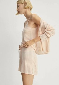 Set od svijetlo ružičastog pletenog loungewear-a koji uključuje top bez rukava s valovitim rubovima i kratke hlače s vezicom, prikazujući teksturirani rebrasti dizajn.
