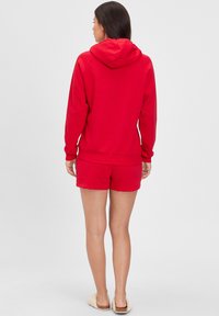 Red sweatshirt with a hood and long sleeves, paired with red shorts. Both are made of a soft fabric, featuring a relaxed fit and ribbed cuffs.
