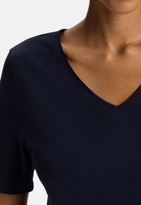 Maglietta a maniche corte blu navy con scollo a V, realizzata in un tessuto morbido, con una superficie liscia e dettagli di cucitura minimi lungo il colletto.