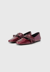 Un paio di eleganti ballerine marrone scuro con punta affusolata, caratterizzate da più cinturini decorati con spuntoni metallici e un dettaglio a catena sulla parte superiore.