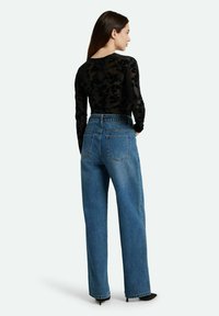Schwarzes Spitze-Oberteil mit langen Ärmeln und floralen Mustern, kombiniert mit hochgeschnittenen blauen Jeans. Die Jeans haben ein gerades Bein und Gesäßtaschen.