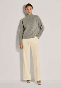 Helles grauer Strickpullover mit hohem Kragen, kombiniert mit crèmefarbenen, weit geschnittenen Cordhosen und hellgrauen Schuhen.