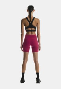Black sports bra with open back design, paired with fitted pink shorts. The shorts feature a smooth texture and a high waistband.