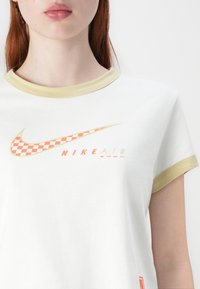 White cotton t-shirt with short sleeves, cream trim, large orange checkered Nike logo, and "NIKE AIR ZOOM" text below.