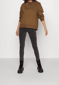 Felpa con cappuccio marrone e tasca frontale, abbinata a jeans skinny grigi e stivali neri con lacci e suola spessa.