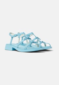 Blue strappy sandals with a block heel, featuring a smooth synthetic finish, minimalist design, and bows at strap intersections.