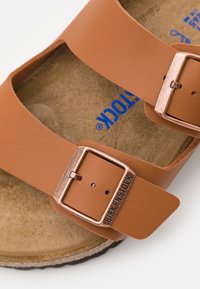 Brown leather sandal with two adjustable straps, metallic buckles, and a contrasting cork footbed. Textured interior for comfort.