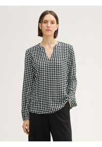 Blusa de patrón en blanco y negro con escote en V, mangas largas y un corte holgado. La tela parece suave con un acabado brillante.