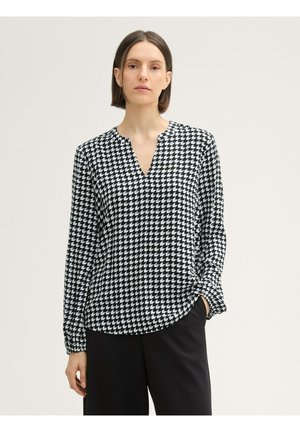 Blusa de patrón en blanco y negro con escote en V, mangas largas y un corte holgado. La tela parece suave con un acabado brillante.