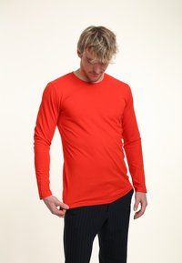 Röd långärmad t-shirt i mjukt tyg, med rund halsringning, slim fit och sidofickor, kombinerad med randiga byxor.