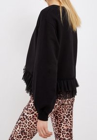 Sudadera negra con un dobladillo de tul con volantes, con mangas largas y un corte holgado, combinada con leggings ajustados de estampado de leopardo.