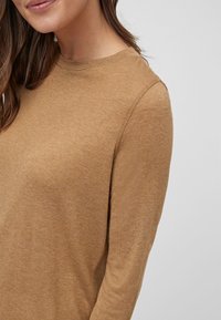 Maglia a maniche lunghe color cammello, realizzata in tessuto morbido e texturizzato. Presenta un collo rotondo e una vestibilità comoda. Nessun motivo o hardware visibili.