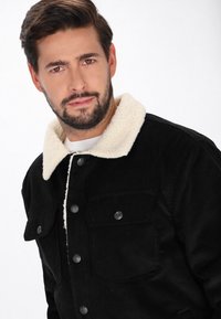 Fekete kordbársony dzseki krémszínű, bolyhos gallérral, két elülső zsebbel és fém gombos záródással. Simajobb textúra, strukturált dizájn.