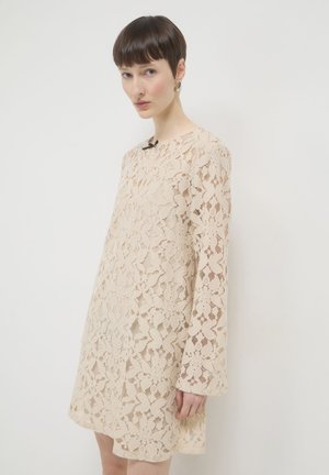 Abito in pizzo beige, con maniche lunghe, motivo floreale e scollatura rotonda. Il materiale appare delicato e textures.