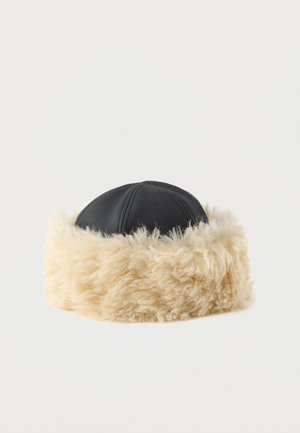 Black faux leather hat with a wide, fluffy beige faux fur band. Round shape, featuring visible stitching on the leather portion.