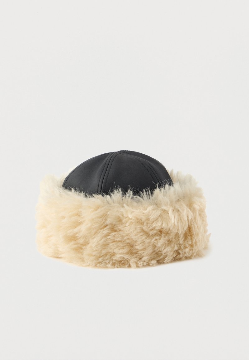 Black faux leather hat with a wide, fluffy beige faux fur band. Round shape, featuring visible stitching on the leather portion.