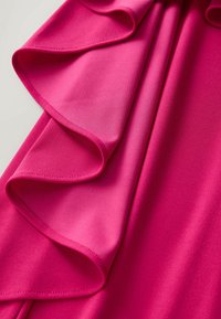 Fuksjowa tkanina o gładkiej teksturze z falbaną, elegancko zwieszona. Kolor jest żywy i jednolity w całej powierzchni.