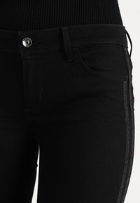 Svarta jeans i denim med en åtsittande design, med en glänsande strukturerad rand längs sidan. Inkluderar en silverknapp och standard framfickor.