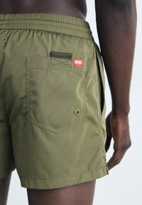 Shorts de bain verts en matériau léger, dotés d'une taille élastique, d'une poche latérale et d'un patch logo rouge Diesel à l'arrière.