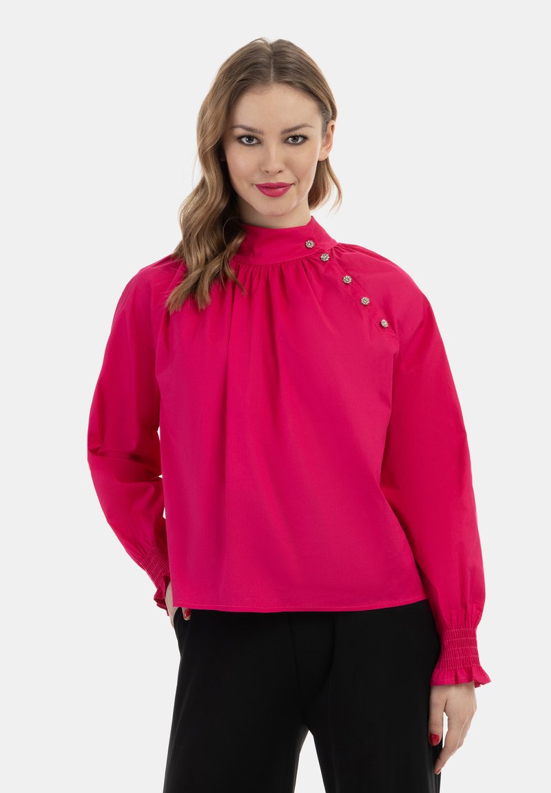 Fuchsia bluse med høj hals, draperet front og knapdetaljer på skulderen. Lange ærmer med elastiske manchetter. Glat stoftekstur.
