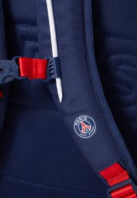 Navy blue backpack featuring textured fabric, red hardware, and a circular logo displaying "Paris Saint-Germain". Adjustable straps included.