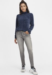 Tengerészkék kötött pulóver magas gallérral, világosszürke szűkített farmerrel és színes sportcipőkkel párosítva.