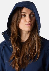 Navyblauwe hooded jacket met rits en drukknoopsluitingen, met een gladde textuur en verstelbare capuchon, gedragen over een donkere top.
