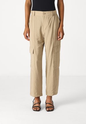 Beige cargo bukser med en let glans, featuring en knaplukning, plisseringer og sidelommer, parret med sorte strop sandaler.