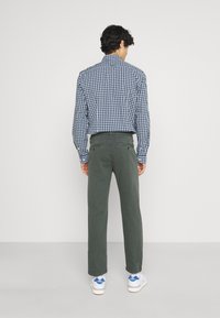 Camicia quadrettata blu e bianca, pantaloni verdi e sneakers bianche con dettagli blu. L'outfit presenta una vestibilità comoda ed è adatto per un look casual.
