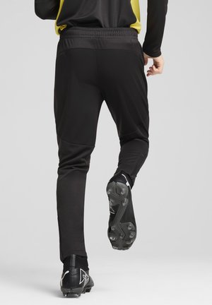 Schwarze Sportleggings mit Slim-Fit, elastischem Bund und strukturierten Einsätzen. Kombiniert mit schwarzen Fußballschuhen mit Stollen.