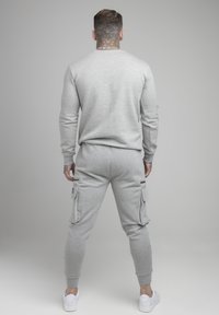 Sudadera gris y pantalones de chándal hechos de material suave. Los pantalones de chándal cuentan con dos bolsillos laterales cargo y puños ajustados. Zapatillas blancas completan el conjunto.