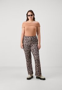  Béžový top s jedním ramenem a řasením, v kombinaci s béžovými a černými kalhotami s leopardím potiskem. Modelka má na sobě černé sluneční brýle a světlé boty.