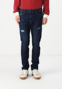 Mørkeblå denimjeans med slim fit, som har slittede lapper og falming, supplert med et klassisk femlommesdesign.