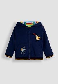 Sudadera con cremallera en color navy que presenta un forro de rayas coloridas, detalles en amarillo y diseños bordados de un caballero y un dragón. Tejido suave de mezcla de algodón.