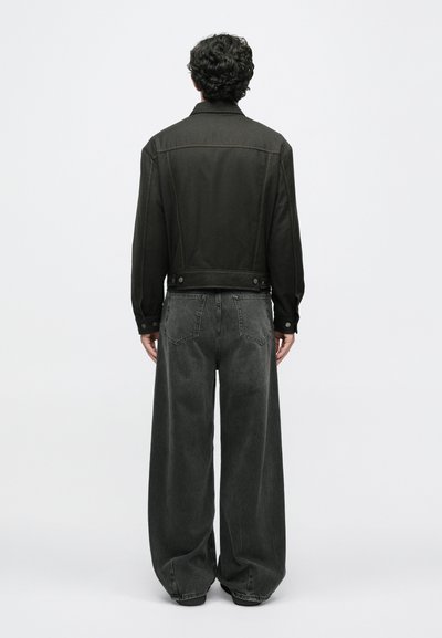 Jachetă din denim negru cu cusături și butoane vizibile, asortată cu pantaloni din denim gri închis, largi. Outfit-ul are o croială relaxată și detalii minime.