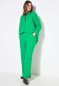 Ensemble en coton vert en deux pièces avec une coupe décontractée, comprenant une chemise boutonnée et un pantalon assorti avec des poches latérales et un tissu texturé.