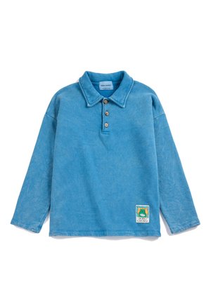 Polo bleu à manches longues avec trois boutons et un petit patch coloré près de l'ourlet sur fond blanc.