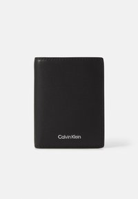 Svart lær lommebok med en jevn tekstur, minimalistisk design, sammenleggbar form og sølvfarget Calvin Klein-logo på forsiden.