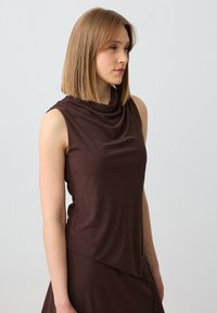 Top senza maniche marrone con scollatura drappeggiata. Tessuto liscio, forma aderente e orlo asimmetrico con dettagli testurizzati.