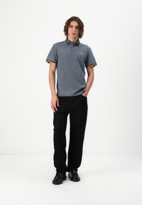 Grå polo skjorte med krave, der har gule og sorte striber, parret med sorte bukser og sorte sko. Enkel design og tætsiddende form.