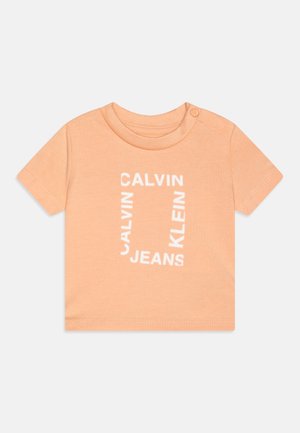 T-shirt pêche à manches courtes avec col rond et fermeture par boutons-pression. Présente un texte blanc avec le motif répétitif "CALVIN KLEIN JEANS".