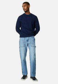Sudadera navy con cuello redondo, combinada con pantalones cargo de mezclilla azul claro que cuentan con dos bolsillos frontales. Zapatillas negras completan el conjunto.