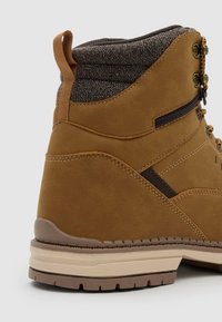 Bota de senderismo de cuero marrón con cuello acolchado de tela, cremallera lateral, cierre de cordones en la parte frontal, suela reforzada y lazo trasero para facilitar su colocación.